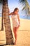 blonde girl in lace closeup leans on palm trunk on beach