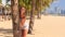 blonde girl in lace looks out of palm puts hand on hip on beach