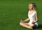 Blonde girl meditating on green grass. Beautiful young woman seating in Yoga pose of lotus in the park