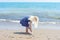 Blonde girl playing at the beach, writing in the sand with a feather