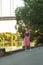 Blonde girl in purple top and light pink skirt in sneakers with a small red shoulder bag smiles. summer evening. embankment.