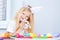 Blonde girl in rabbit ears on head and little bunny in her hands. Colorful eggs and markers on table. Prepearing for Easter and