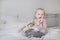 Blonde girl sitting on a bed with pink flowers and ribbon, portrait of a cute baby on a light background