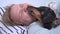 Blonde girl sleeps with cute dachshund in embrace on lazy weekend, close up. Naughty dog licks owners face and tries to