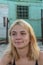 A blonde girl in a swimsuit smiles against the background of temporary buildings for displaced persons.