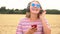 Blonde girl teenager young woman wearing blue sunglasses in a field listening to music on her cell phone and wireless headphones