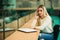 Blonde girl use phone in library. sudent sist on stool by the window