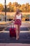 Blonde with glasses crosses the train tracks at the station with her red suitcase