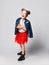 Blonde kid girl with funny buns in red skirt, white t-shirt and denim jacket over shoulder poses having fun