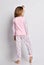 Blonde kid girl in stylish shirt and pants pyjamas with flower print pattern stands back to camera