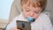 A blonde kid watches cartoons on his smartphone