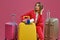 Blonde lady in red pantsuit, white blouse. She touching hair, sitting among colorful suitcases, holding passport and