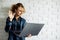 Blonde with laptop in her hands standing against white brick wall.