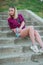 Blonde in light blue high-rise shorts, red plaid shirt, sitting on the stairs outside, looks to the left. vertical photography