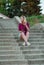 Blonde in light blue high-rise shorts, red plaid shirt, sneakers sitting on the stairs outside, looks to the left. vertical