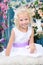 Blonde little girl in white dress sits on white