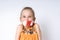 Blonde little model in orange blouse posing isolated on white. Her mouth tied by white and red warning tape. Coronavirus