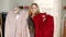 Blonde longhaired girl playfully choosing between pink and red blouse on hangers comparing them in front of a mirror