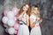 Blonde and redhead. Two young charming girlfriends at the party with balloons. On gray textured background