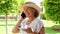 blonde senora woman, 50-55 years old, in a hat and a white dress, talks using a smartphone and holds a cup of coffee in