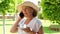 blonde senora woman, 50-55 years old, in a hat and a white dress, talks using a smartphone and holds a cup of coffee in