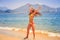 blonde slim girl in bikini expresses joy jumps tip toe on sand