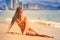 Blonde slim girl in bikini sits stretched leg on wet sand