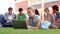 Blonde student using laptop with classmates sitting behind on grass