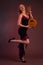 The blonde in Studio is dancing, standing on one leg in a black dress with a mandolin in her hand