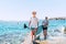 Blonde teenage son with father surfers smiling and carrying the stand-up paddleboard with a paddle on the bright sunny day noon.