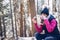 A blonde tourist sits on a tree stump, drinks hot tea and eats a hamburger on a mountain trail.