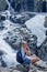 A blonde tourist is sitting on a rock above the Siklawa waterfall in the Polish Tatra Mountains.