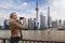 A blonde tourist woman takes pictures of the urban skyline of Shanghai