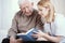 Blonde volunteer reading book to senior man in nursing home