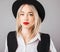 Blonde woman with big red lips in black hat portrait. Grey background