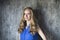 Blonde woman in blue blouse staying in front of dark wall and keep smiling