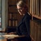 Blonde woman dressed in black tweed suit reading book in library