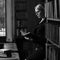 Blonde woman dressed in black tweed suit reading book in library