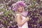 Blonde woman enjoying in a spring garden with blooming lilacs with bouquet, lilac flowers hair style.