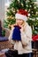 Blonde woman in funny hat at Christmas tree looks what a surprise gift in a bag.