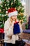 Blonde woman in funny hat at Christmas tree looks what a surprise gift in a bag.