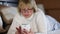 Blonde woman in glasses with white smartphone lying on the bed