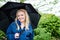 Blonde woman holds a black umbrella on an overcast rainy day in a lush garden