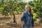 Blonde woman in jeans with a basket handing on her arm ready to pick organic fruits and vegetables in an orchard