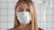 Blonde woman medical mask face looking anxiously to camera while quarantining Coronavirus COVID-19 virus.