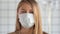 Blonde woman medical mask face looking anxiously to camera while quarantining Coronavirus COVID-19 virus.