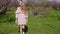 Blonde woman in pink dress walks by a blooming garden with trees