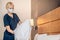 Blonde woman in a protective mask making bed in a hotel room