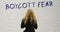 Blonde woman reads boycott fear written on the white wall