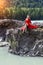 Blonde woman in red dress  sits stretching her long legs on the rock stones on banks of Katun river against background of